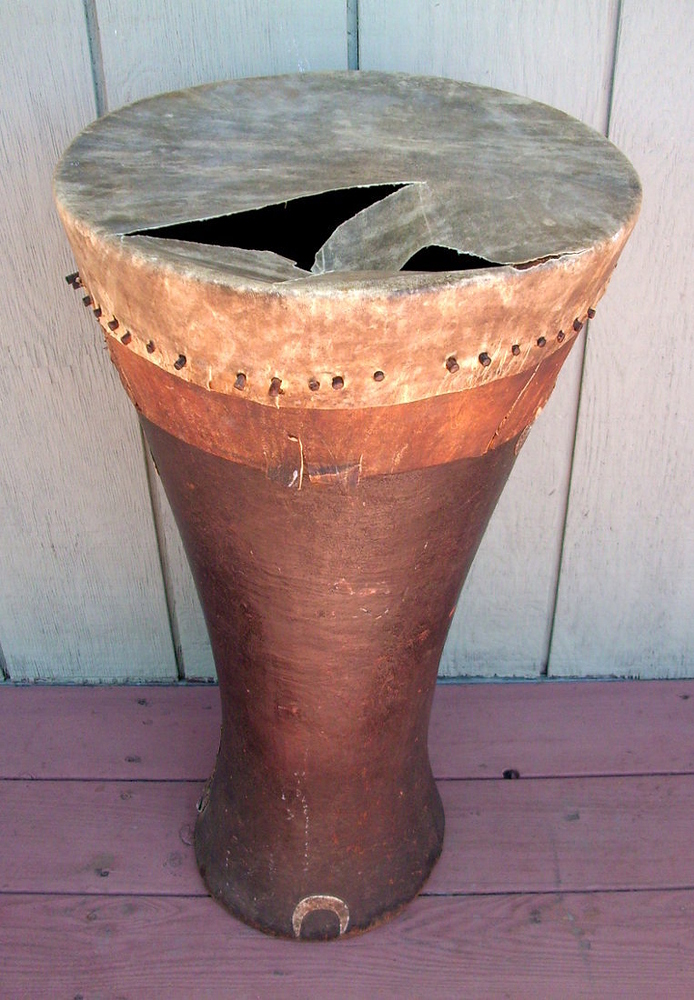 An african drum with pegs holding torn skin on body